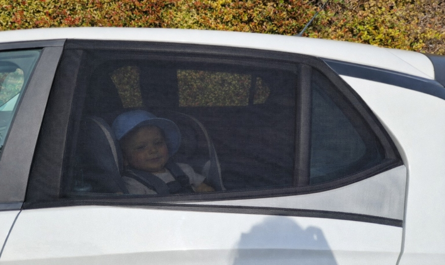 Baby in rear car seat behind Qualizzi mesh sunshade with window partially open for airflow and UV protection
